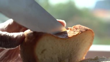 Bir dilim ekmek kes. Elleri tek kullanımlık eldivenlerde, bıçakları ekmekle kesiyorlar. Taze ekmek pencereye yakın bir masada, sabah güneşiyle aydınlatılıyor. Sağlıklı beslenme ve geleneksel pişirme kavramı.