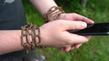 Demir zincirlere sarılı bir adamın elleri akıllı telefonu tutar. Modern bir insanın internet ya da sosyal ağlara bağımlılığı kavramı.