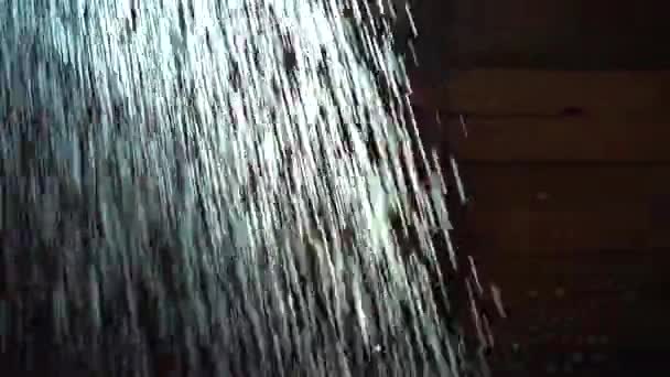 L'acqua cade in corsi d'acqua sottili. La doccia cade da vicino, retroilluminata dalla luce del sole su uno sfondo scuro — Video Stock