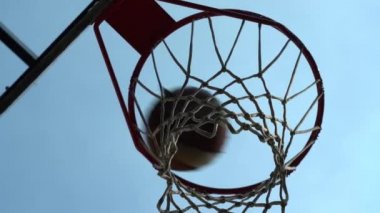 Eski bir basketbol topu çemberden kameraya doğru düşüyor. Top ringe çarpıyor. Top ringe çarptı, üzerinde mavi gökyüzü olan yeni bir açık hava çemberi. Alt manzara. Popüler bir açık hava oyunu. Yavaş