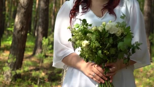Une fille en robe blanche tient un beau bouquet de fleurs dans ses mains par une journée ensoleillée d'été dans le parc. Gros plan. Mouvement lent — Video