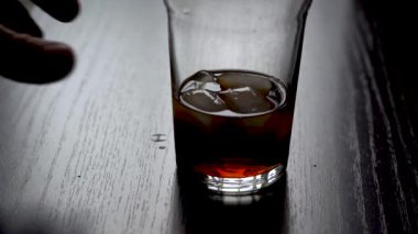 Bir bardak soğutucu iç. El, siyah bir masanın üzerinde buz küpleri olan bir bardak kola alır. Ağır çekim. Pencereden gündüz lambası