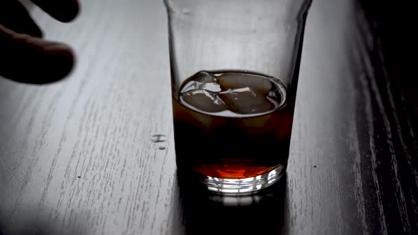 Take a glass of a cooling drink. Hand takes a glass of cola with ice cubes on a black table. Slow motion. Daytime backlight from the window — Stock Video