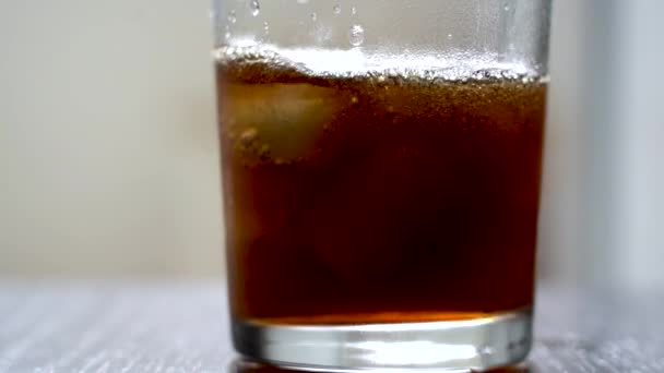 Pour cola into a glass with ice. Cold refreshing cola is poured into a glass with ice on a light background. Natural daylight from the window. Slow motion — Stock Video