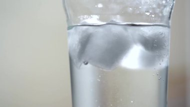 Puslu bir bardakta buzlu su. Suda küçük kabarcıklar. Hafif arkaplan. Gün ışığı. Yakın plan.