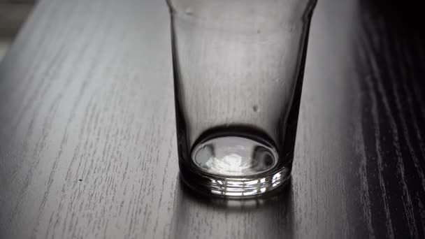 Ice fall into a glass. Slow motion. Close-up shot of ice cubes falling into empty clear glass on dark bar counter, slow motion. Empty glass with ice cubes on wooden table on a black background. — Stock Video