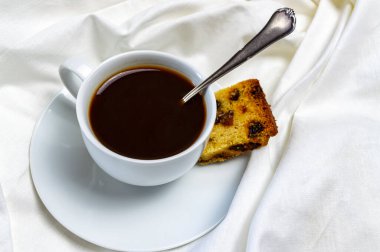 Bir fincan kahve ve yatakta bir parça kek kahvaltısı.