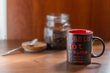 Bir fincan kahve ve kahve çekirdekleri, ahşap bir masa üzerinde duran. Arka plan şeffaf bir kavanoza kahve