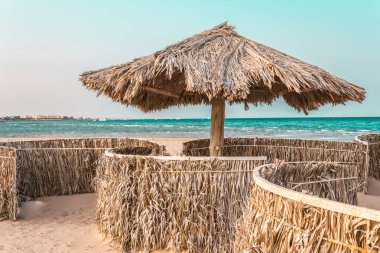 denizin kenarında palmiye ağaçlarından doğal malzemelerden yapılmış plaj şemsiyeleri