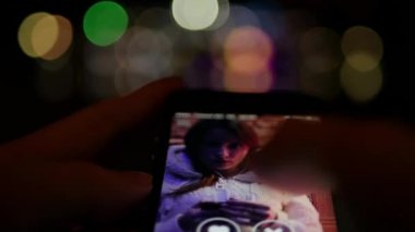 Sosyal keşif için akıllı telefon uygulaması kullanmak - karşı cinsle çevrimiçi çıkmak - arka planda bokeh ışıkları olan gece görüntüleri