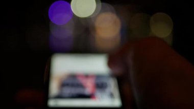 Gece akıllı telefon taraması - bulanık odaklanmış konsept görüntüler - arka planda kentsel bokeh ışıkları olan sosyal ağ kullanımı