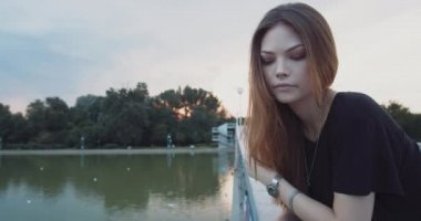 Burun piercing ile sıkılmış genç kadın gün batımında bir nehir köprüsünde sıkılmış