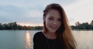 Neşeli genç kız bir nehir kıyısında yavaş hareket gün batımında gülümsüyor