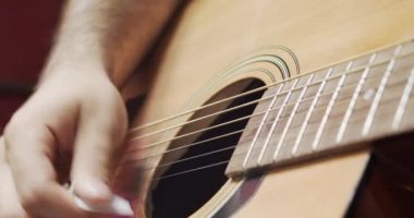 Gitarist akustik gitarın tellerini koparıyor. Yakın plan.