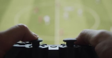 Kullanıcı bir oyun konsolundan geniş ekran üzerinde bir joystick kontrolörüyle futbol oyunu oynuyor