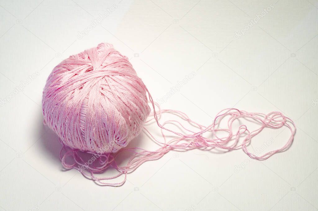 A tangle of pink knitting threads on a white textured background. The concept of handmade
