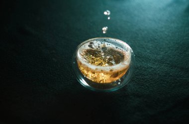 Yeşil çay bir cam fincana dökülür, su sıçratır ve kabarcıklar