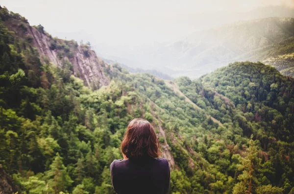 Genç bir kız dağların manzarasının tadını çıkarıyor. Doğanın arka planında turist gezgini.