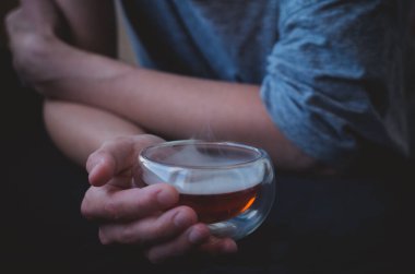 Kadın eli sıcak çay bardağını tutar. Bulanık arkaplanı olan rahat bir fotoğraf..