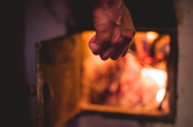 Bir adamın elinin, ocağa odun atarken ve kömürleri karıştırırken yakın çekimi. Geleneksel ısınma kavramı