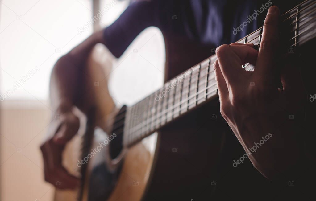 The girl plays the guitar in the room.Dim light from the window