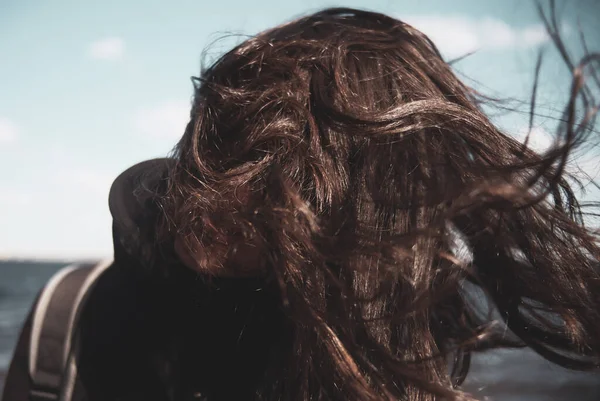 Rüzgarlı bir havada deniz kıyısında saçları çıkan bir kız..
