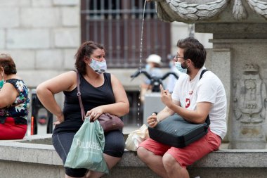 Madrid, İspanya - 8 Ağustos 2020: Madrid şehrinde gün batımında gezen turistler ve aylaklar. İnsanlar kendini Covid-19 'dan korumak için maske takıyor.