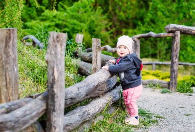 Sevimli bebek bebek kız, şehir dışında bir parkta ahşap bir çit ayakta