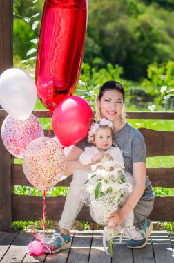 Anne ve küçük kızı zarif bir beyaz balonlar ve lilyum buketi ile onların ilk Doğum elbise. Holiday Park. Mutlu gülümseme aile.