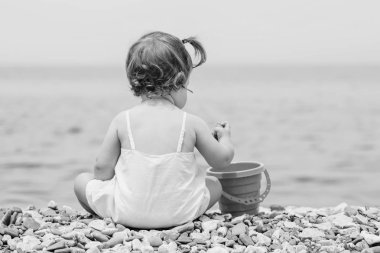 Küçük bir bebek bir çakıl plajı üzerinde oturur ve çakıl (siyah ve beyaz ile çalış )
