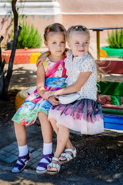 Zwei Kleine Schulmädchen Auf Dem Kindergartenspielplatz Sitzen Auf Der Bank — Stockfoto