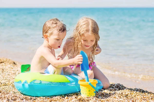 小孩子们拿着水桶和橡胶圈在沙滩上玩耍 图库照片