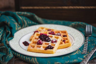 Geleneksel Belçika waffleları taze ahududu ve reçel ile yeşil ve kahverengi arka planda.