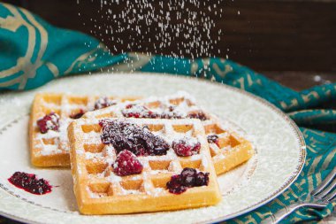 Siyah zemin üzerinde şeker tozu bulunan ev yapımı Belçika waffleları ile beyaz tabak. Eski ahşap masanın üzerinde şeker tozu. Koyu kırsal tarzda. yumuşak odak