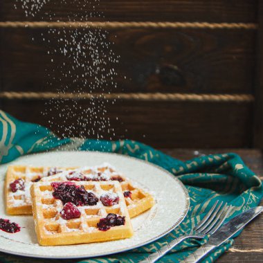 Siyah zemin üzerinde şeker tozu bulunan ev yapımı Belçika waffleları ile beyaz tabak. Eski ahşap masanın üzerinde şeker tozu. yumuşak odak