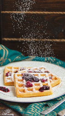 Siyah zemin üzerinde şeker tozu bulunan ev yapımı Belçika waffleları ile beyaz tabak. Eski ahşap masanın üzerinde şeker tozu. yumuşak odak