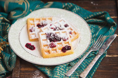 Siyah zemin üzerinde şeker tozu bulunan ev yapımı Belçika waffleları ile beyaz tabak. Eski ahşap masanın üzerinde şeker tozu. yumuşak odak