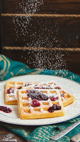 Siyah zemin üzerinde şeker tozu bulunan ev yapımı Belçika waffleları ile beyaz tabak. Eski ahşap masanın üzerinde şeker tozu. yumuşak odak