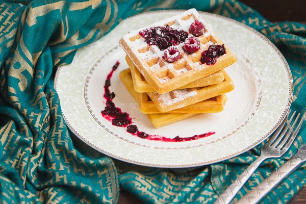 Beş waffle istiflenmiş, beyaz tabakta ahududu ile süslenmiş..