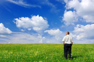 Yeşil alan, mavi gökyüzü ve arka plan beyaz bulutlar üzerinde duran işadamı