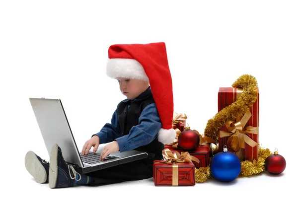 小男孩在圣诞老人帽与笔记本电脑和圣诞礼物在白色背景 — 图库照片