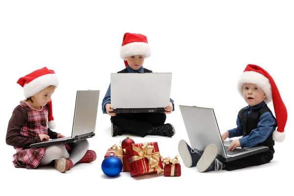 两个男孩和一个女孩在圣诞老人帽子与笔记本电脑在白色背景 被隔绝 — 图库照片