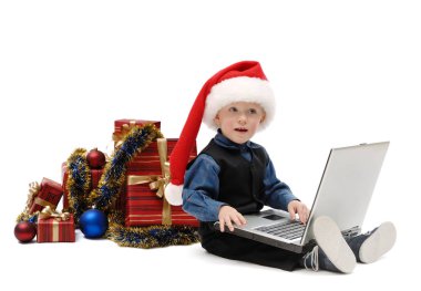 Bir dizüstü bilgisayar ve izole beyaz arka plan üzerinde Noel hediyeleri Noel Baba şapkalı küçük çocuk