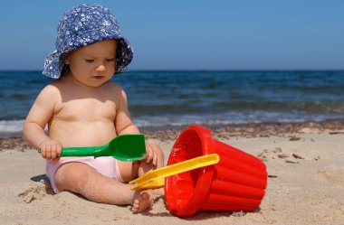 Sahilde, mavi gökyüzü arka planda çalmaya mavi şapkalı küçük kız