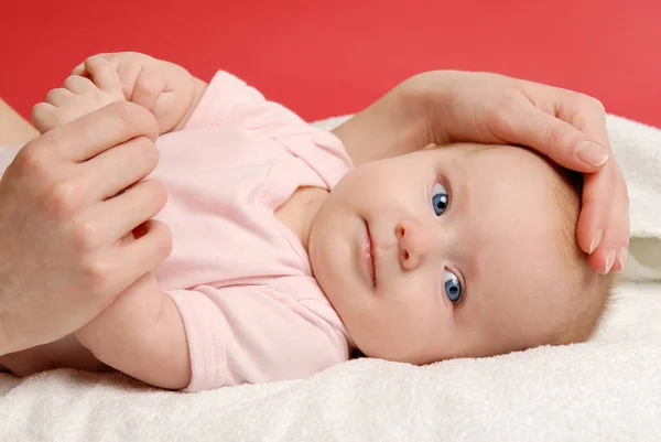 Meisje van de baby liggen op een witte deken en haar moeder's hand — Stockfoto
