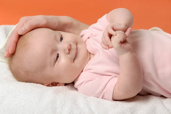 Meisje van de baby liggen op een witte deken en haar moeder's hand — Stockfoto