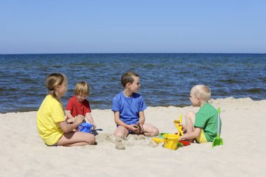 İki kız ve iki erkek renkli t-shirt içinde bir kumlu b oturan