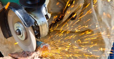 Demirci grindering yukarıdan bir açı değirmeni tutan metal bir plaka vurdu. Demirci grindering metal bir plaka