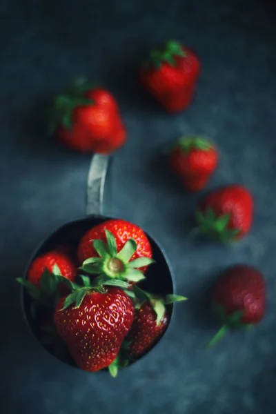 Mogna jordgubbar spridda runt en järnmugg. Mörkt foto — Stockfoto