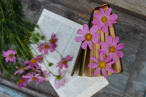 Ahşap arka planda bir buket pembe yabani çiçekli kapalı bir kitap.